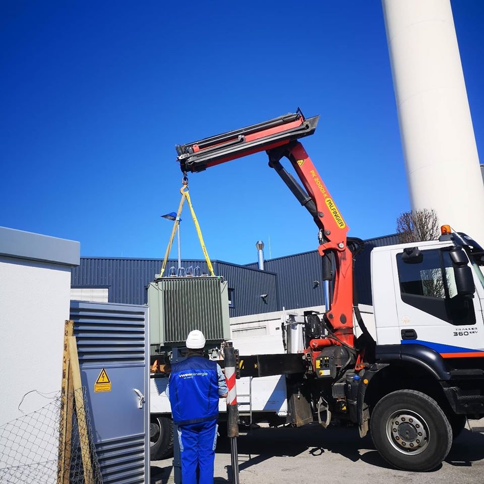 Transformator wird mit Lkw-Kran neben einer Trafostation angehoben