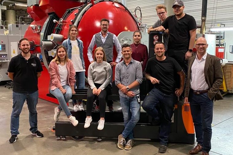Team der BURKHARD Group in der Produktion Teamgruppe steht vor großer roter Industrieanlage in Produktionshalle