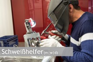 Mitarbeiter mit Schweißhelm arbeitet an Metallbauteil mit Schweißgerät