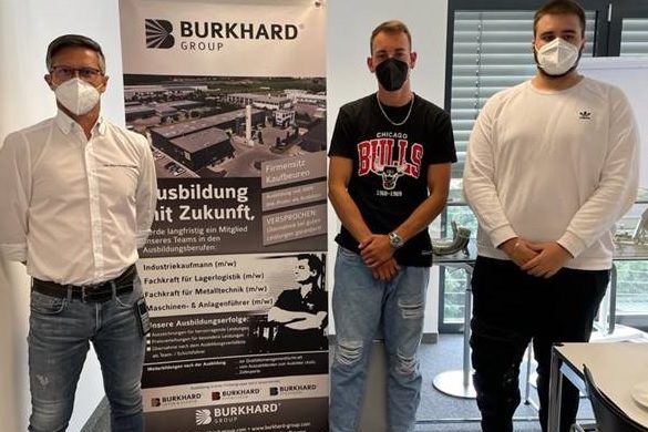 Drei Männer mit Mundschutz stehen neben BURKHARD Ausbildungs-Rollup im Büro